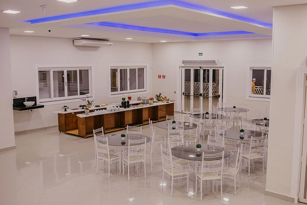 Refeitório claro com mesas redondas brancas e balcão de buffet