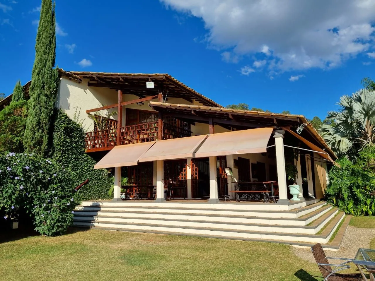 Casa principal de madeira e tijolo, com varanda e escadaria, entre árvores