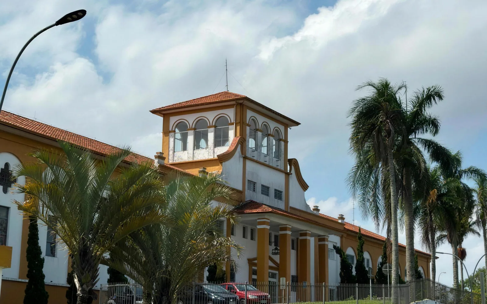 Fachada da Elibrè vista da rua, com a torre e o jardim de palmeiras