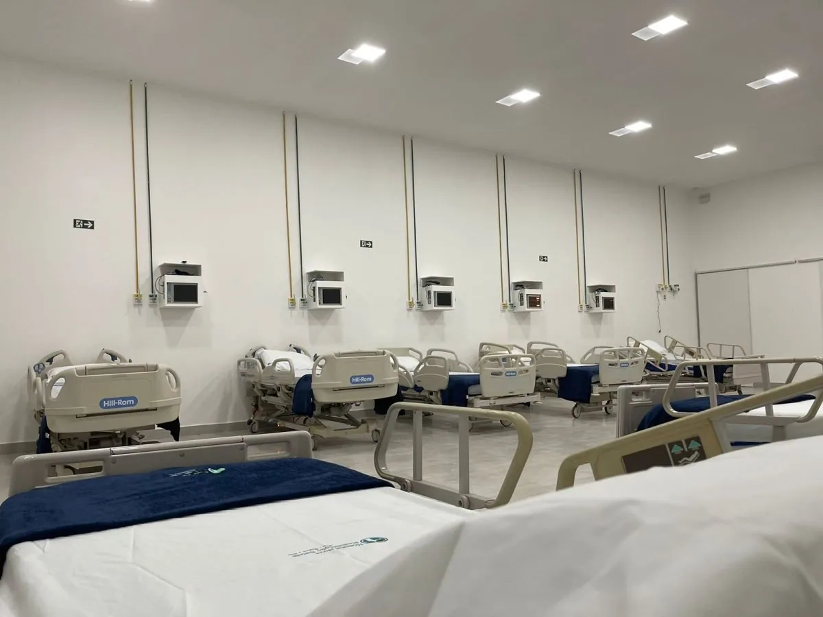 Enfermaria ampla com camas hospitalares enfileiradas e roupa de cama azul