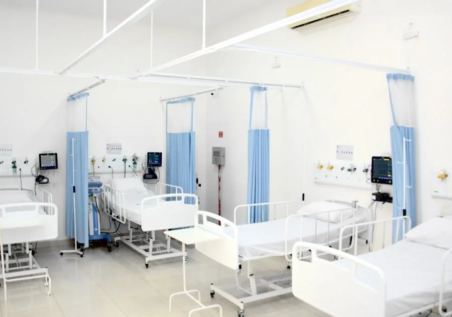 Enfermaria com camas hospitalares, cortinas azuis e painéis de gases na parede