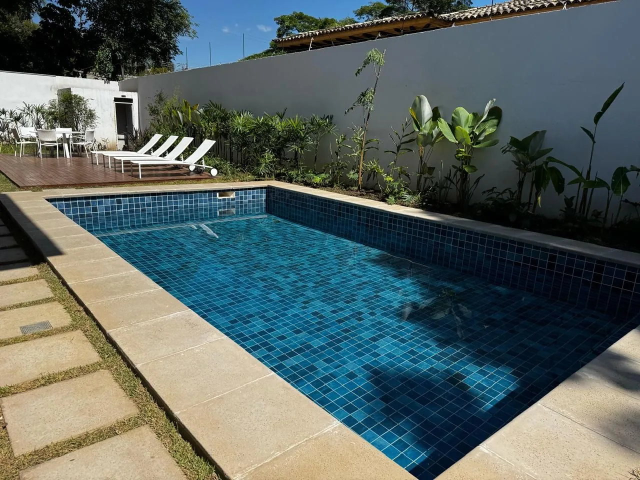 Piscina externa com deck, espreguiçadeiras e jardim tropical