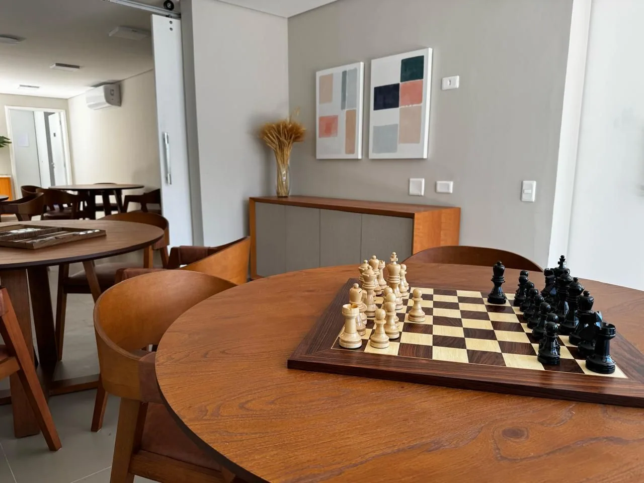 Sala de refeições com mesas redondas de madeira e tabuleiro de xadrez